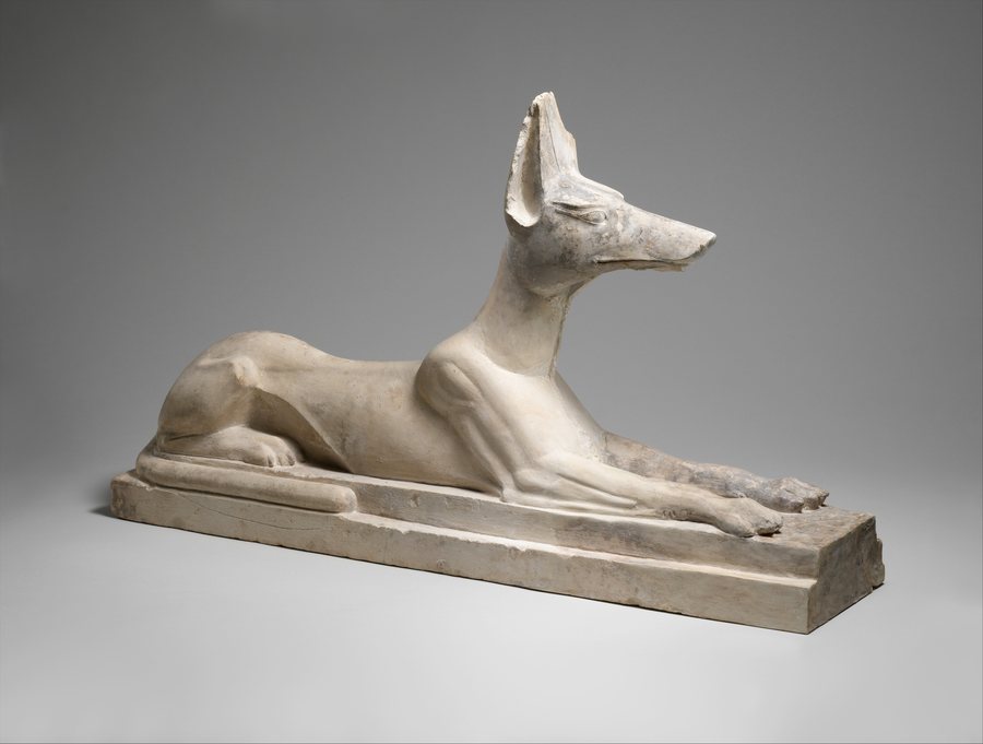 Limestone statue of Anubis as a recumbent dog with pricked ears and wrinkled brow